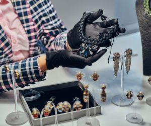 Close-up photo of a jewelry worker presenting a costly necklace with gemstones in a luxury jewelry store.